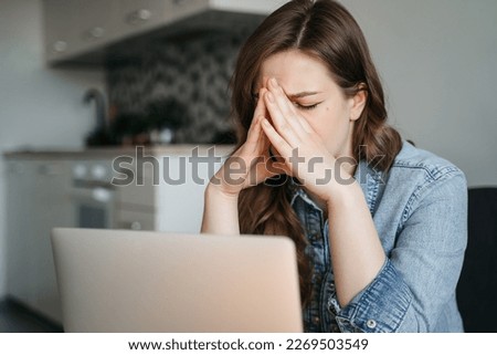 Female freelance with eyes closed is massaging head temples with suffering face expression. Tired and worn out from online work young woman sitting in front laptop holding head. High quality photo