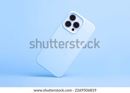 iPhone 14 and 13 Pro Max in light blue soft silicone case falls down back view, phone cover mockup in monochrome colours isolated on blue background