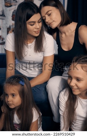   Staged photo. A lesbian couple and their children are having a good time at home.  While the kids are watching a cartoon, the parents are cuddling affectionately.                             