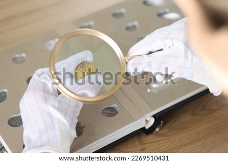 Close-up of woman numismatist examining coin with magnifier. Female looks at coins through loupe. Numismatic collection review Royalty-Free Stock Photo #2269510431