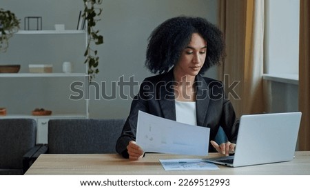 African teacher worker business woman work with graphics documents at home office check documentation enter financial data to laptop processing online information paying bills in computer banking app Royalty-Free Stock Photo #2269512993