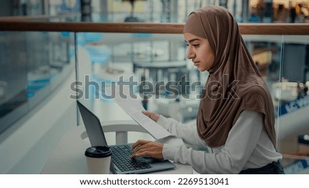 Young female entrepreneur arabian muslim woman in hijab businesswoman freelancer work with papers business contracts check financial documents paying bills in online banking app e-commerce on computer Royalty-Free Stock Photo #2269513041