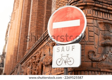Do not enter road sign with the word "SAUF" and a bicycle symbol black and white sign meaning "except" bikes near red brick and carved building in Paris, France on the corner of a french street
