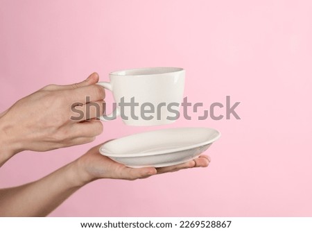 Female hands hold a white ceramic cup with a saucer on a pink background Royalty-Free Stock Photo #2269528867
