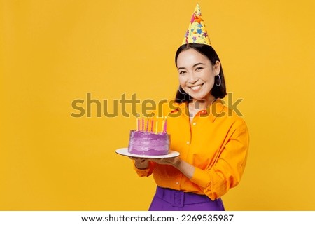 Happy fun smiling young woman wearing casual clothes cap hat celebrating holding in hand purple cake with candles look camera isolated on plain yellow background. Birthday 8 14 holiday party concept Royalty-Free Stock Photo #2269535987