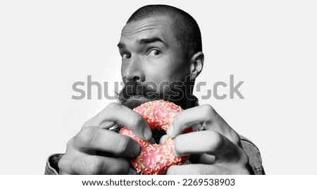 Brutal guy with donut in his hands on gray background. Black and white photo with a color element. The concept of vigor and recuperation. Concept healthy food, junk food, fast carbohydrates.