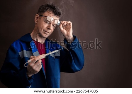 A man with glasses looks at a smoking soldering iron Royalty-Free Stock Photo #2269547035