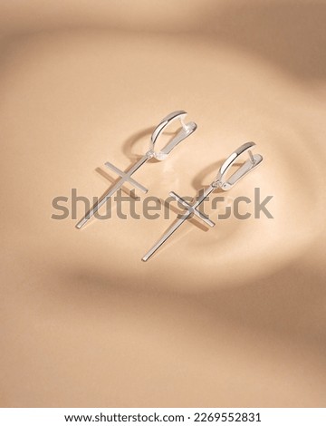 White gold silver earrings with crosses on beige background. Still life and creative photo with shadows.