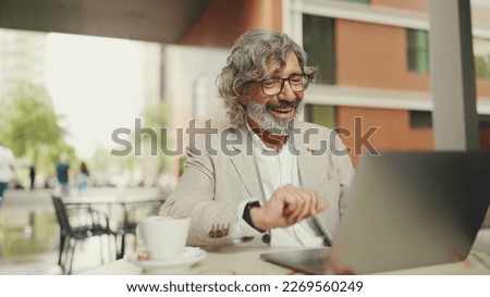 Mature businessman with beard in eyeglasses wearing gray jacket sits drinks coffee in cafe. Middle aged manager successful man working on laptop pc computer sit at cafe outdoors Royalty-Free Stock Photo #2269560249