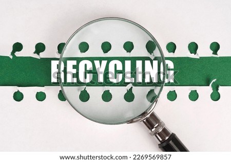 Between two sheets from a notebook on a green strip with the inscription - recycling, there is a magnifying glass. The concept is ecological.