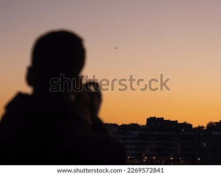 A photographer takes a picture with the buildings and the sunset in the background.