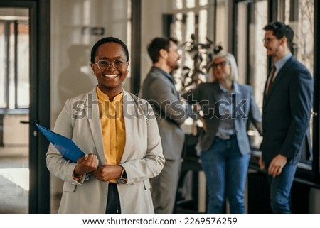 Shot of a businesswoman holding files while standing in the boardroom. Group of people standing in the background. 