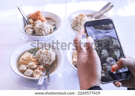 Woman taking a picture of meatball food using a cell phone