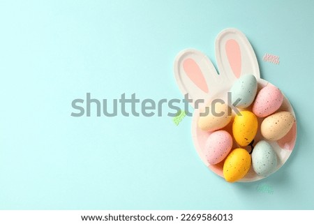 Happy Easter flat lay composition. Top view colorful Easter eggs on plate with bunny ears on pastel blue table.