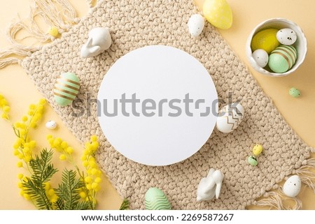 Easter concept. Top view photo of empty white circle bowl with colorful easter eggs ceramic bunnies cloth napkin and mimosa flowers on isolated beige background with blank space