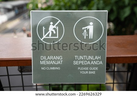 the sign on the crossing bridge .the meaning of the sign Dilarang memanjat and Tuntunlah sepeda is a do not climb  and bicycles must be led.