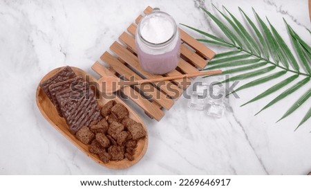 Grape juice and chocolate biscuits on a wooden chopping board, chocolate bowl, chocolate spoon, green leaves close to each other against a white background with a black pattern and the picture is take