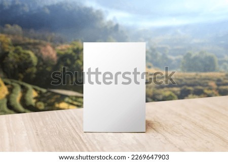 Mock up Label the blank menu frame in Bar restaurant. Stand for booklet with white sheet paper acrylic tent card on table wiht blurred mountain background.  Can inserting the text or picture.