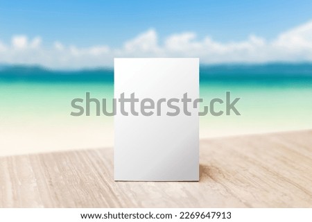 Mock up Label the blank menu frame in Bar restaurant. Stand for booklet with white sheet paper acrylic tent card on table wiht blurred beach background can inserting the text or picture.
