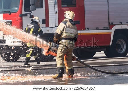 Firefighter - Firemen extinguishing a large blaze, they are standing with protective wear against the background of a fire truck. Firemen using extinguishe