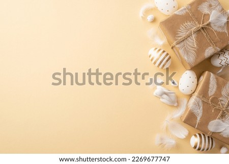 Easter decorations concept. Top view photo of white and gold easter eggs craft paper present boxes with twine bows ceramic bunny and white feathers on isolated beige background with empty space