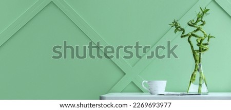 Vase with bamboo branches and cup on table near green wall
