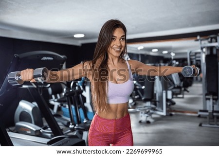 Beautiful fitness woman with lifting dumbbells . Sporty girl showing her well trained body . Well-developed muscles by strength training . Royalty-Free Stock Photo #2269699965