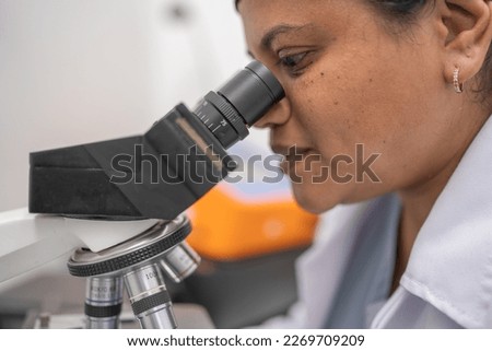 Female lab technician observing and analyzing cells under the laboratory microscope.