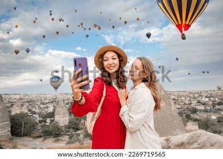 Two friends capture their travels in Cappadocia, Turkey with smartphone selfies amongst beautiful rock formations and hot air balloons. Sharing their experience on social networks.