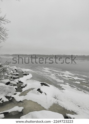 The photo depicts the Dnipro River in winter, frozen under a layer of ice. The serene icy landscape is surrounded by snow-covered trees, creating a picturesque winter scene. The river's blue hues are 