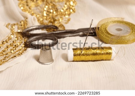 Spool of Gold Thread and Scissors With Thimble on Off White Fabric With Gold Sequins Royalty-Free Stock Photo #2269723285