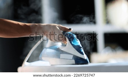 Selective focus of female hand irons white clothes with steam iron on an Ironing board. Push button of steam humidifier, laundry moistening function. Ironing linen using hot steam Royalty-Free Stock Photo #2269725747