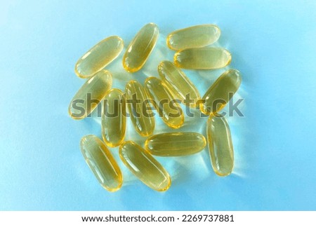 Large yellow pills on blue background, fish oil or omega 3 in the sun, close-up, top view