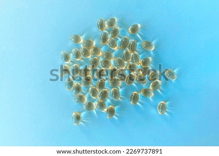 Little yellow pills, capsules, supplements on blue background, vitamin D, D3 or omega 3 in the sun, close-up, top view