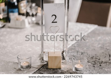 Table number 2. Setting, serving guests closeup. Stands, sign number two. Close up. Wedding setup detail. Festive table covered tablecloth, decorated composition flowers and candles in party area Royalty-Free Stock Photo #2269743745