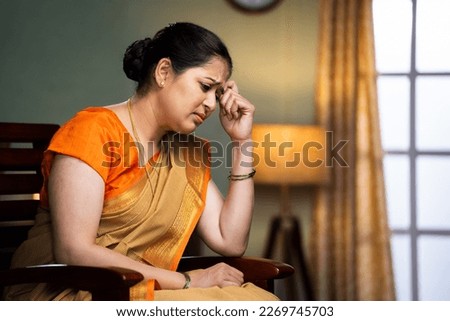 Deep thinking middle aged woman while sitting on chair at home - concept of unhappy, loneliness and worried or lost Royalty-Free Stock Photo #2269745703