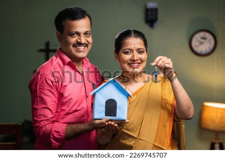 Happy smiling couple showing new house keys by toy home while looking camera - concept of new home purchasing, home loan and investment. Royalty-Free Stock Photo #2269745707