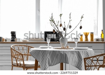 Vase with tree branches and Easter eggs on dining table in kitchen