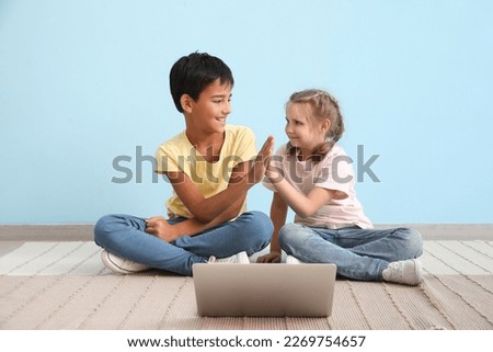 Little boy and girl watching cartoons on laptop near blue wall
