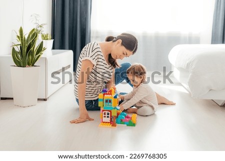 Laughing mother and little daughter  playing colorful  blocks, constructing tower, sitting on warm floor with underfloor heating, family enjoying leisure time together Royalty-Free Stock Photo #2269768305