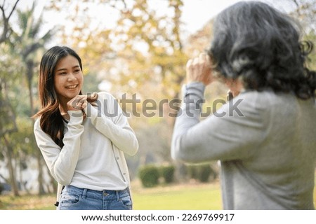 Happy Asian grandma taking a picture of her lovely granddaughter with a retro camera while strolling in the green park together.