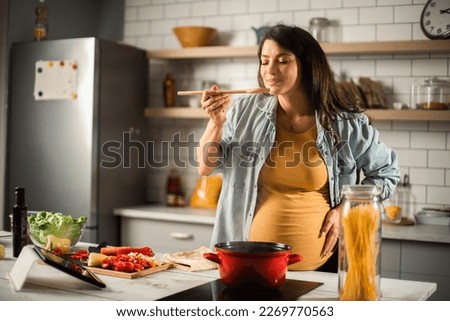 Beautiful pregnant woman preparing delicious food. Smiling woman cooking pasta at home. Royalty-Free Stock Photo #2269770563