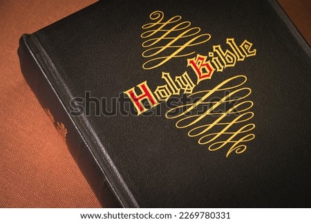 Holy Bible, black cover, brown background. Gold and red letters.