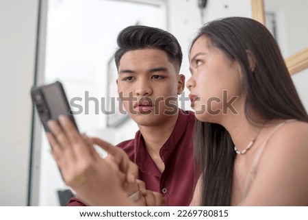 A young woman confronts her boyfriend over suspicious messages or racy photos of another woman on his phone. A man's guilty reaction after caught cheating. Infidelity concept. Royalty-Free Stock Photo #2269780815