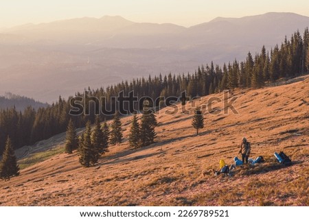 Hillside with forest and resting travelers landscape photo. Nature scenery photography with mountains silhouette. Ambient light. High quality picture for wallpaper, travel blog, magazine, article