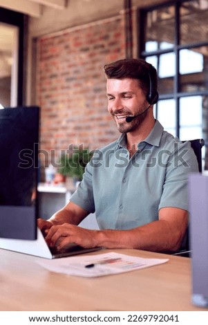 Businessman Wearing Headset At Computer In Customer Support Centre Royalty-Free Stock Photo #2269792041