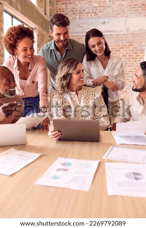 Multi-Cultural Business Team Meeting Around Laptop In Busy Office Royalty-Free Stock Photo #2269792089