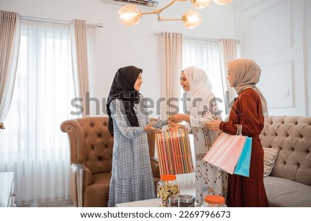 two women in veils give paper bags to the host woman in the living room during Eid celebration