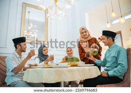 wife serves drinks to the family when breaking the fast at the dining table Royalty-Free Stock Photo #2269796683