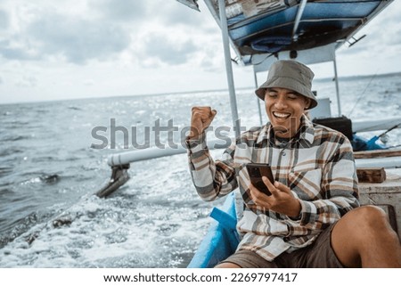 excited angler using cell phone while sitting resting on fishing boat Royalty-Free Stock Photo #2269797417